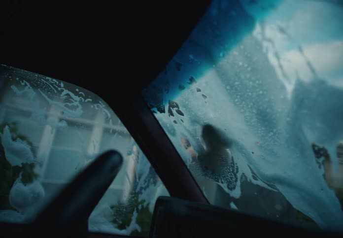 Interior car shot of a man washing the soapy windshield with a sponge in slow motion