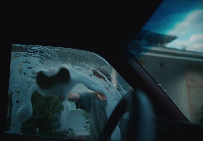 Interior car view of a determined young man meticulously washing the soapy windshield in his driveway