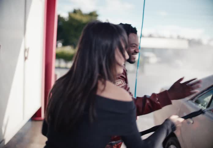 A group of diverse friends playfully dance and laugh while washing their car together at a car wash in slow motion