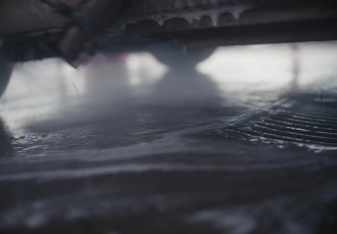 Slow motion close-up of soapy water and suds flowing across a concrete floor into a drain at a car wash