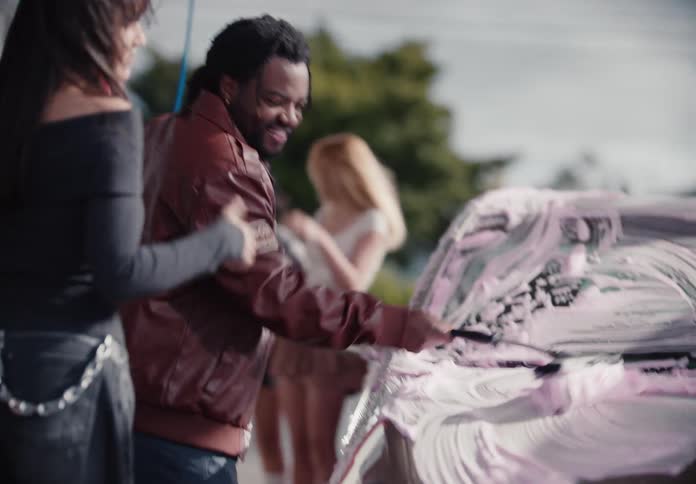 A stylish group of diverse friends have a fun time laughing and washing their car with pink foam in slow motion