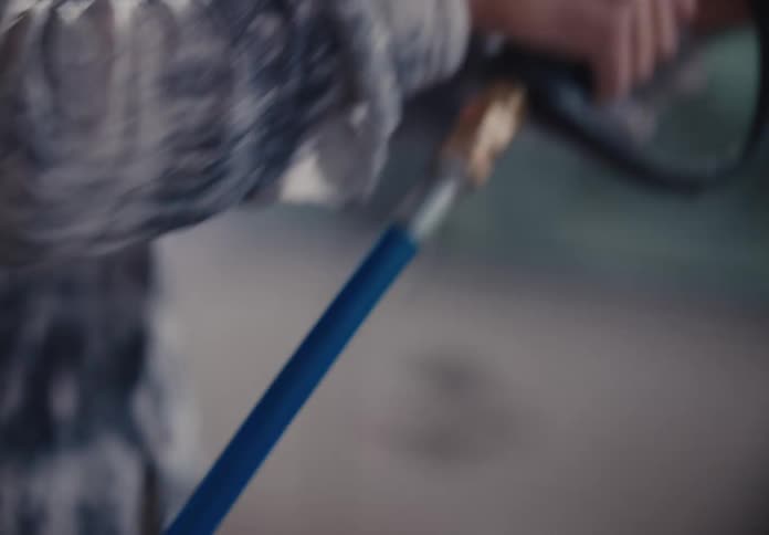 A slow-motion close-up of a young woman's hands holding a pressure washer before the camera reveals her smiling face