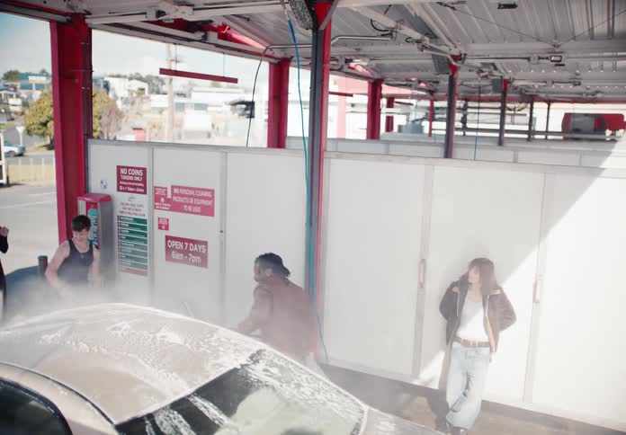 A group of friends playfully washes a car with a high-pressure hose and soap at a self-service car wash