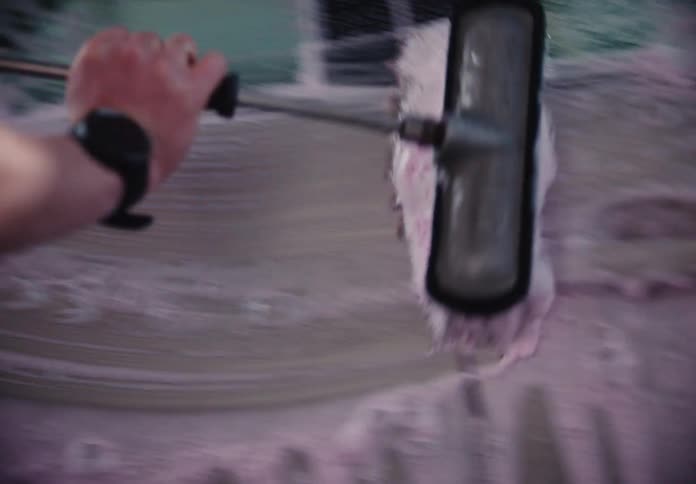 A close-up slow-motion shot shows a person scrubbing a car with a long-handled brush and pink soap foam