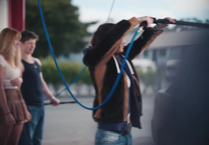 A group of young friends smiles and laughs while using a pressure washer to clean their car at a self-service car wash