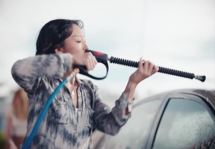 Stylish young women have fun together washing a car at a self-service car wash in slow motion