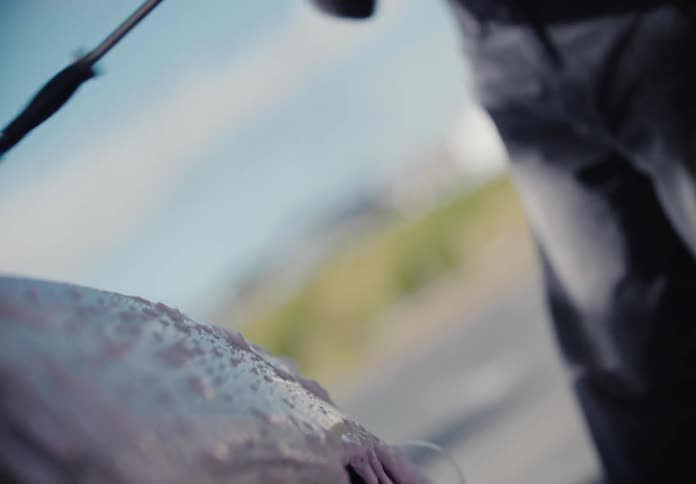 A close-up, slow-motion, and out-of-focus view shows a person washing a car with purple soap and a pressure washer