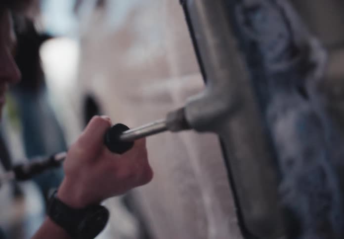 A close-up slow-motion shot of a young man scrubbing the side of a soapy car with a long-handled brush at a car wash