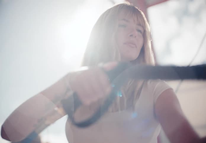 A young woman uses a pressure washer in slow motion at a sun-drenched self-service car wash