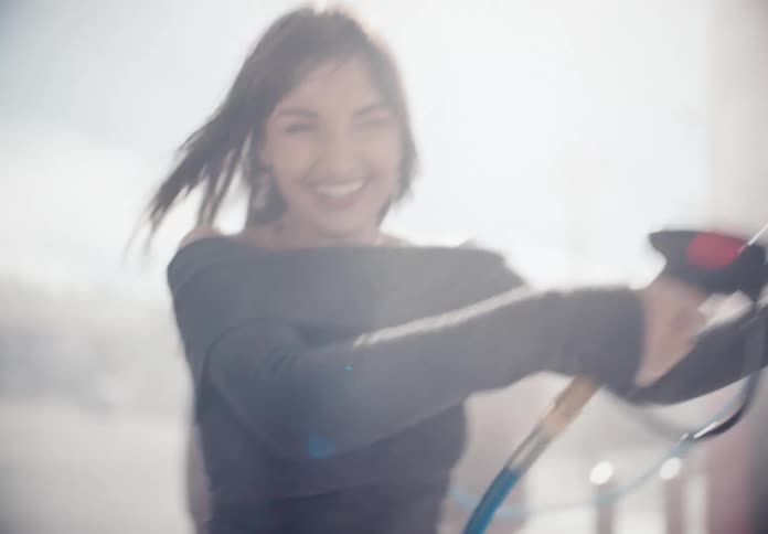 A close-up of a smiling woman's face transitions to her playfully pressure washing a car at a self-service car wash in slow motion