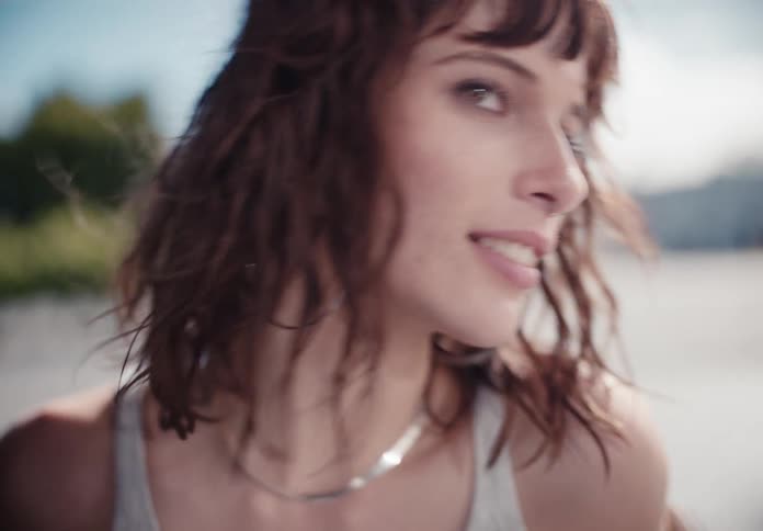 Close-up slow-motion portrait of a smiling young woman with curly brown hair blowing in the wind outdoors