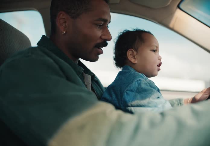 A young African American father holds his adorable toddler on his lap while driving his car on a sunny day