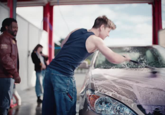 A diverse group of energetic young friends have fun washing a car together at a self-service car wash on a sunny day