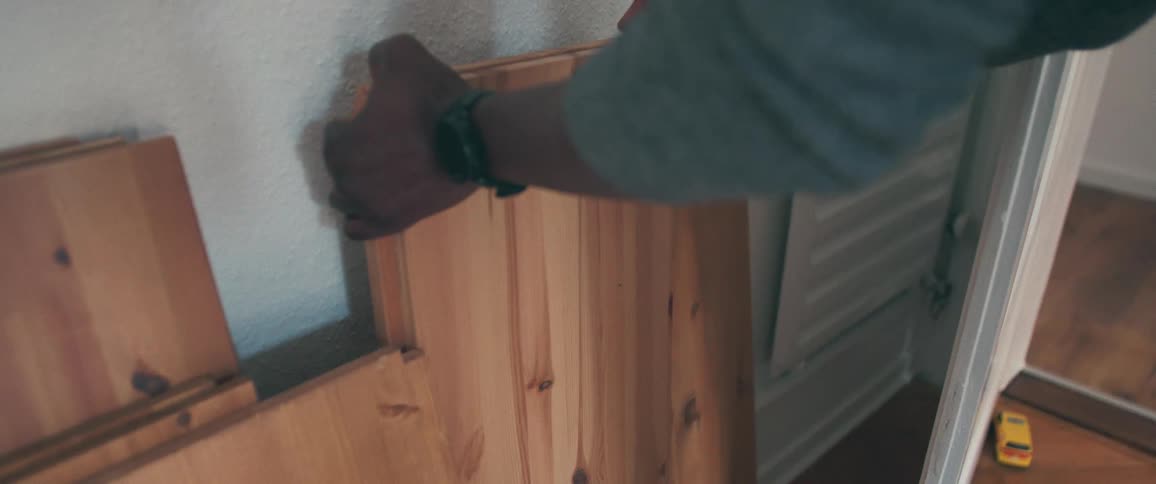 Close up shot of a man's hands putting together pieces of a flat-pack pine furniture unit indoors