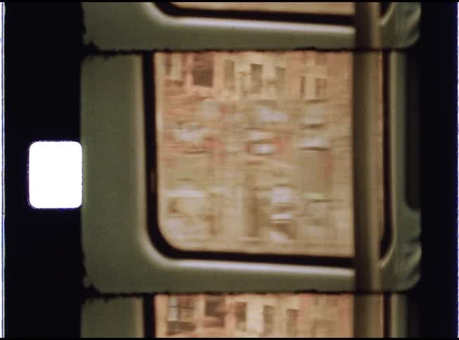 A close-up of a Super 8 film strip showing the view of city buildings and graffiti from a fast-moving train window