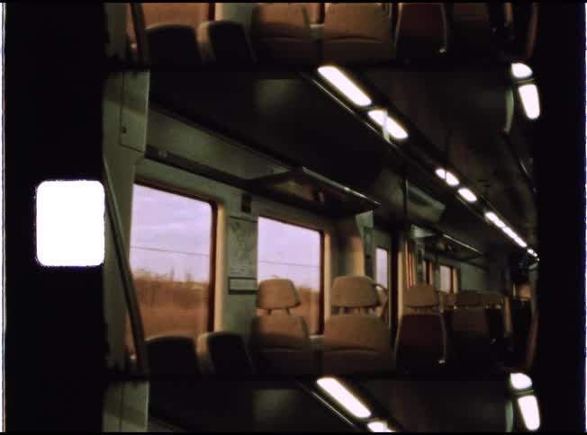 A vintage film view from inside an empty, moving train car as the landscape passes by the window