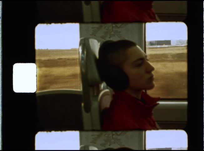 A young person with a buzzcut and headphones gazes out the window while traveling on a train, shot on vintage film