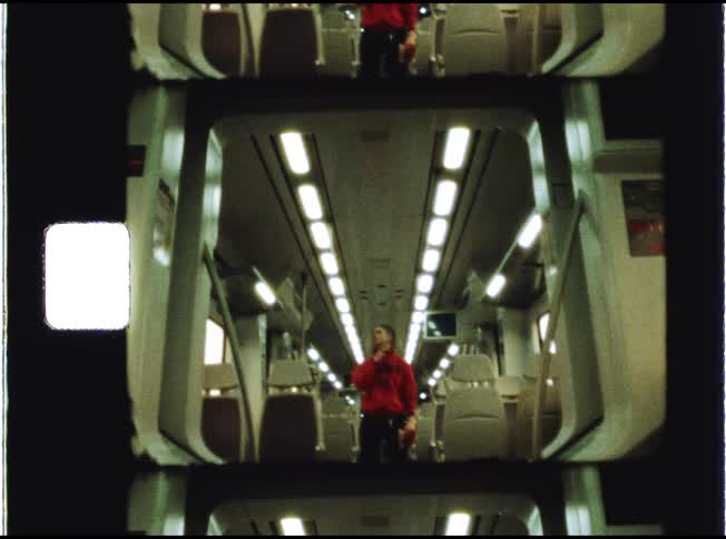 Vintage film footage captures a solitary figure in a red hoodie standing in the aisle of a deserted, modern train