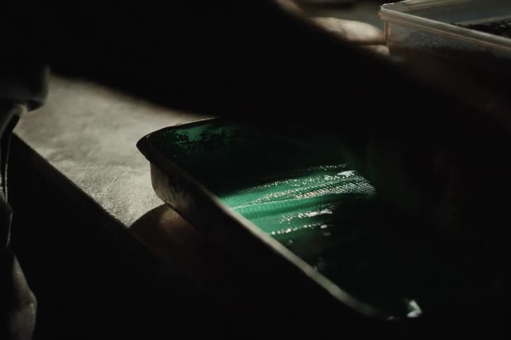 A baker expertly shapes a loaf of bread before placing it into a greased green baking pan