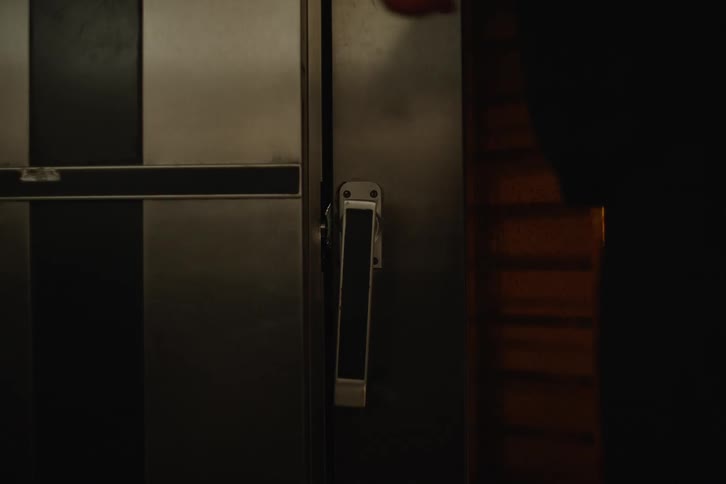 A person opens the heavy metal door of a large industrial oven in a dimly lit commercial kitchen