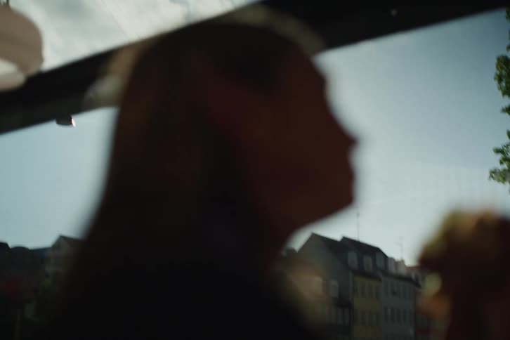 Soft-focus silhouette of a person drinking a beverage while traveling through a sunlit city