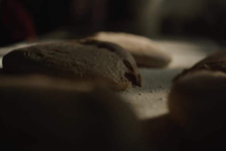 A baker gently sprinkles flour over raw loaves of bread on a wooden board in slow motion