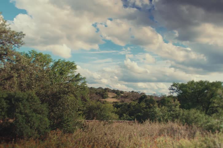 A tranquil landscape scene with rolling hills and trees under a partly cloudy sky