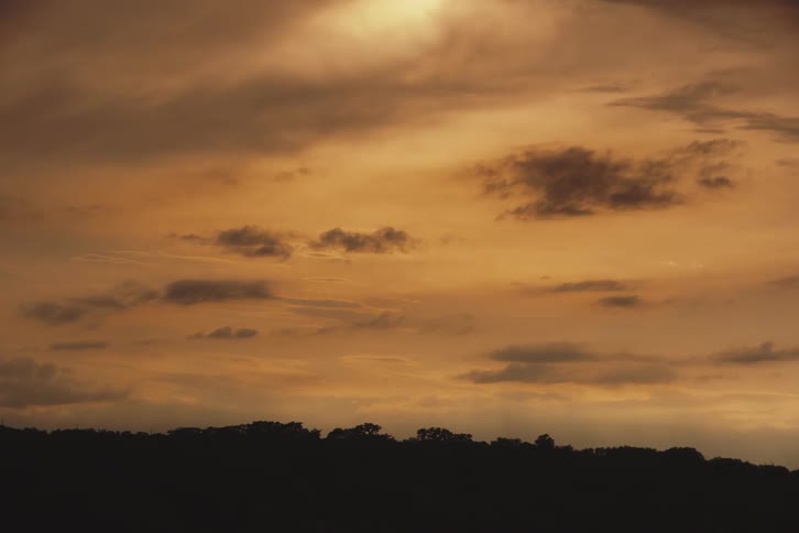 The last light of day casts a warm golden glow across a cloudy sky above a silhouetted landscape