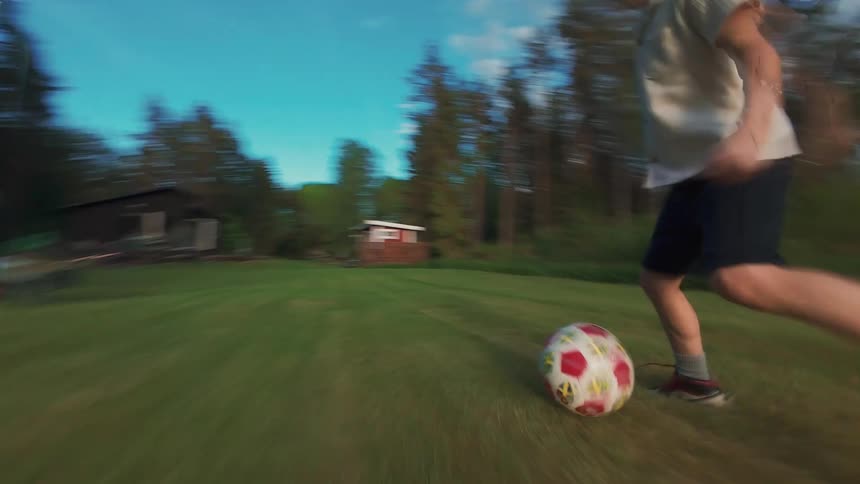 Energetic tracking shot follows a young boy dribbling a soccer ball across a lush green lawn on a sunny day