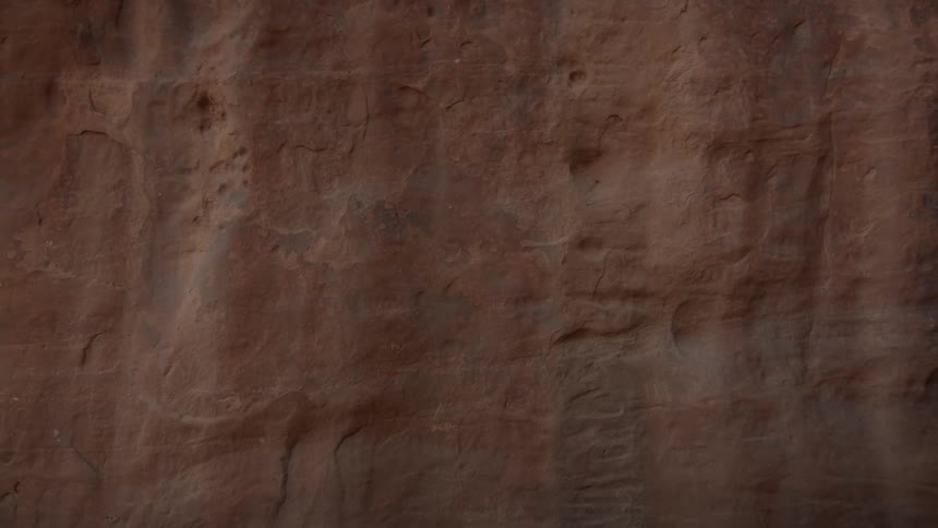 A close-up shot reveals the intricate details of ancient petroglyphs carved into a weathered red rock wall
