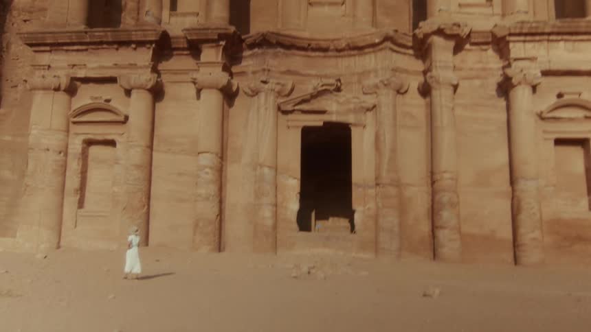 A woman in a white dress stands in awe before the magnificent ancient Monastery (Ad-Deir) carved into the rock in Petra, Jordan