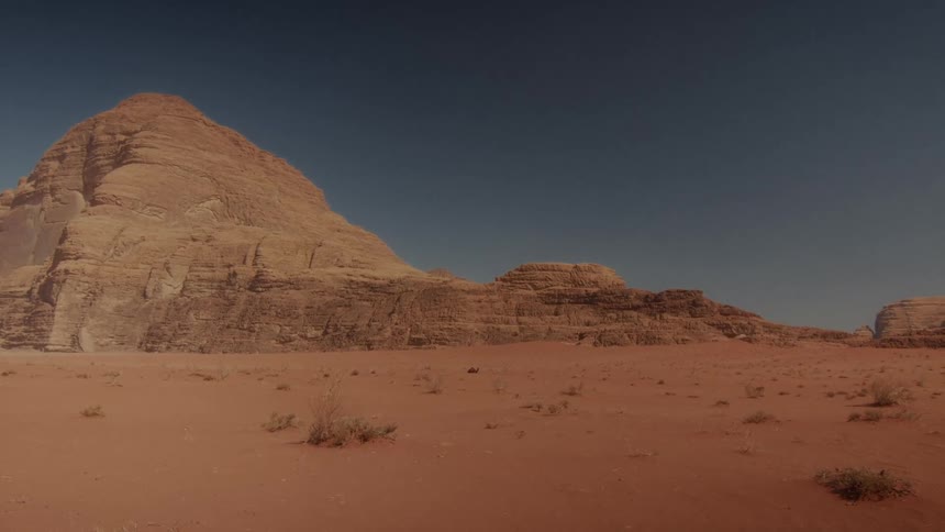 A static wide shot captures the vast, arid landscape of the Wadi Rum desert with its iconic red sand and sandstone mountains