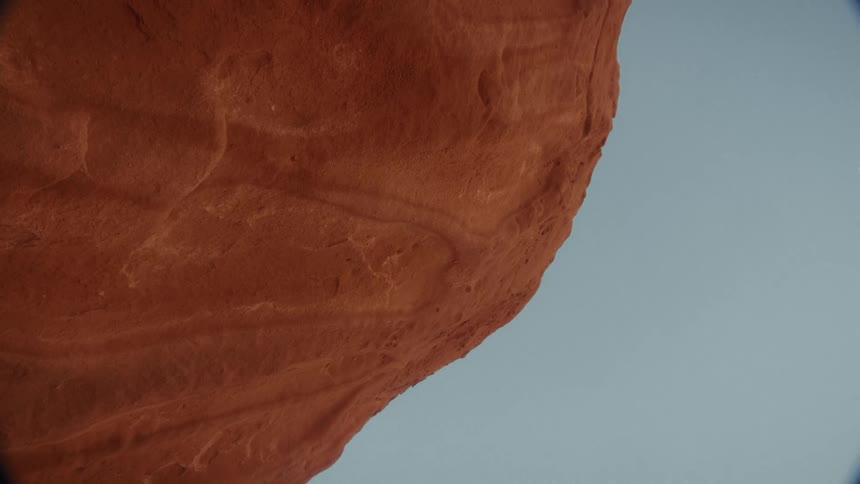 A vertical close-up of a textured red rock formation against a clear blue sky