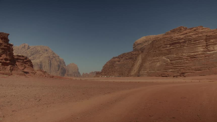 Time-lapse of an expansive red rock desert valley with mountains under a clear blue sky