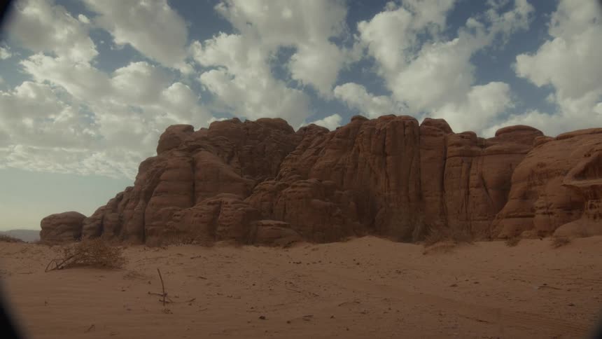 Timelapse of white clouds moving across a blue sky above a majestic red rock formation in a vast desert
