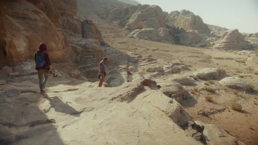 A group of friends carefully hike through a rocky, sun-drenched desert canyon on an adventure