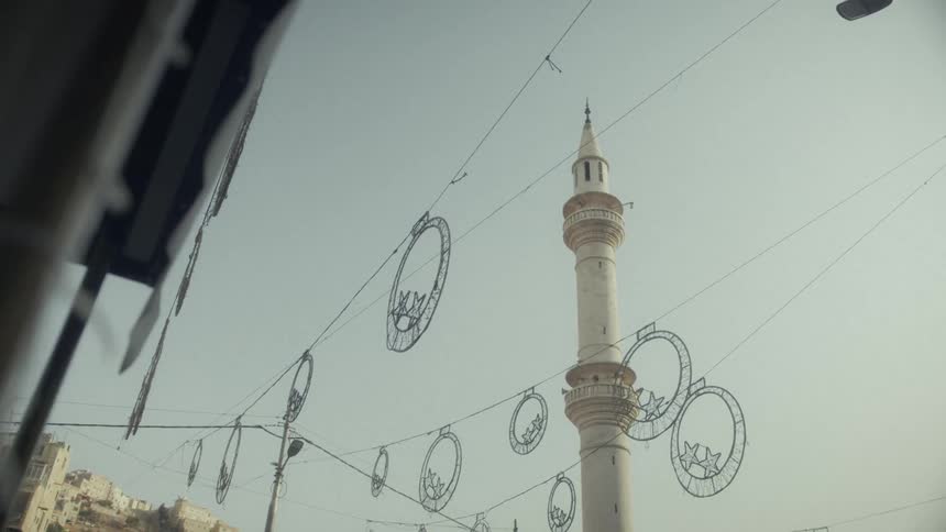 Slow reveal of a minaret with festive decorations hanging overhead on a city street