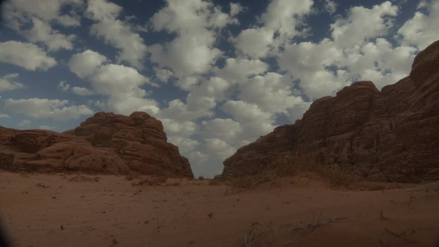 A low-angle time-lapse shows fluffy white clouds drifting over a majestic desert canyon on a sunny day