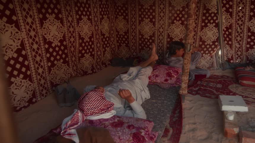 An older man wearing a keffiyeh and a young boy relax inside a traditional Bedouin tent