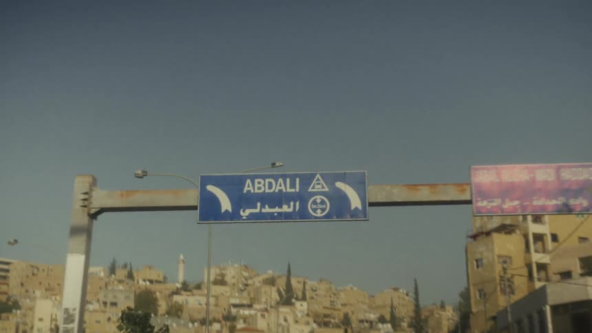 A slow-motion point-of-view shot from a car driving under a road sign for the Abdali district in Amman, Jordan