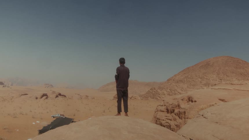 A lone person stands on top of a rocky outcrop, looking out over the vast desert landscape