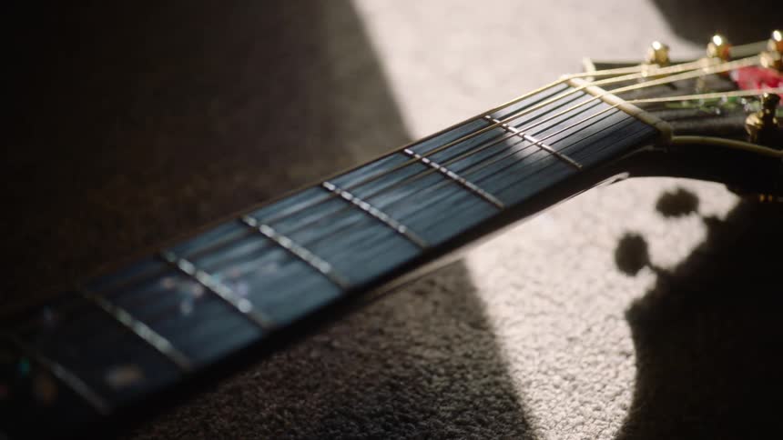 A slow pan up the fretboard and neck of a beautifully inlaid acoustic guitar resting in a beam of sunlight