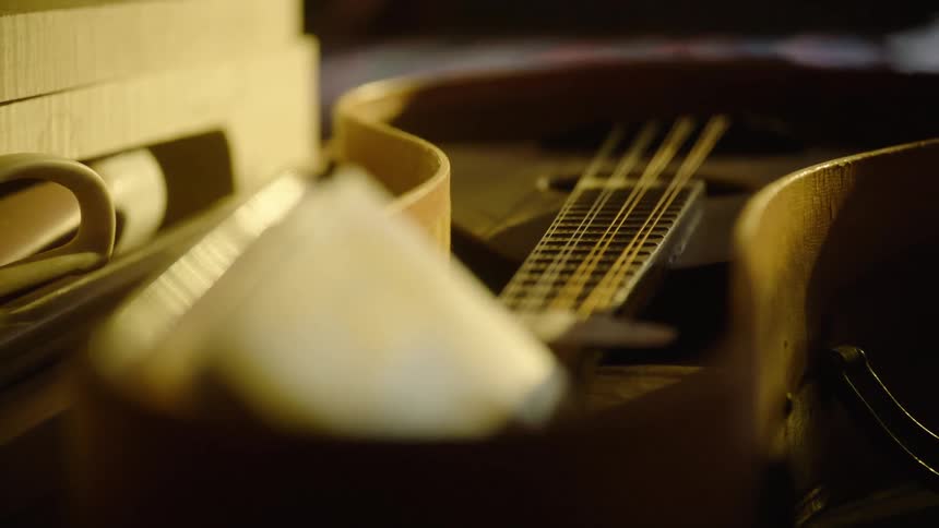 A slow focus pull reveals a vintage mandolin resting in its case in a warm, dimly lit room