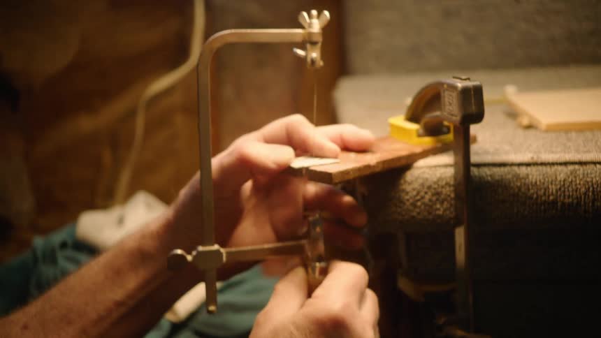 A craftsman's hands carefully use a small hand saw to precisely cut a piece of wood in a workshop
