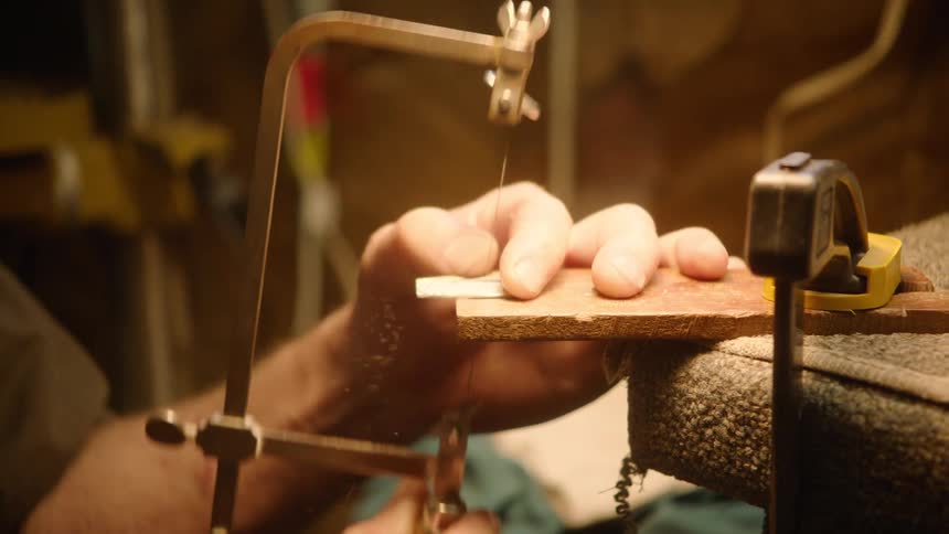 A skilled artisan meticulously cuts a small piece of material with a fine hand saw in a warmly lit workshop
