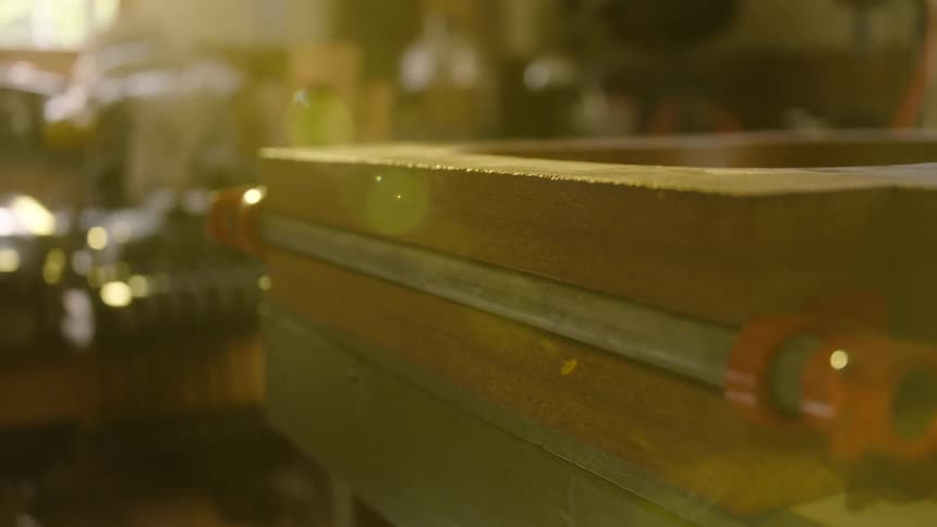 A wooden frame is clamped together on a workbench in a sunlit, dusty workshop