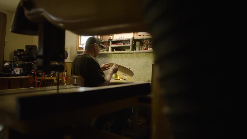 A focused woodworker carefully crafts a project at his workbench in a dimly lit, personal workshop