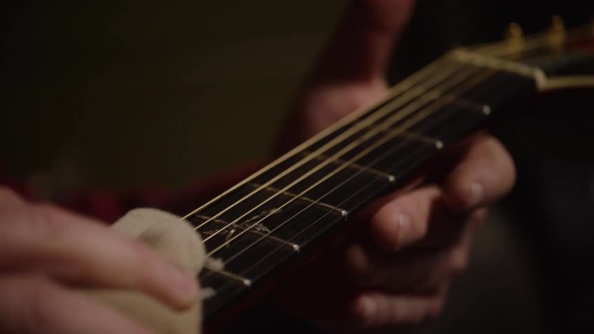 A musician carefully wipes down and cleans the fretboard and strings of a beautiful acoustic guitar with floral inlays