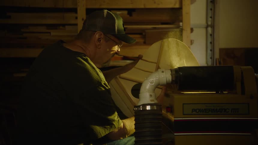 A focused craftsman carefully sands the wooden body of a handmade acoustic guitar in his workshop
