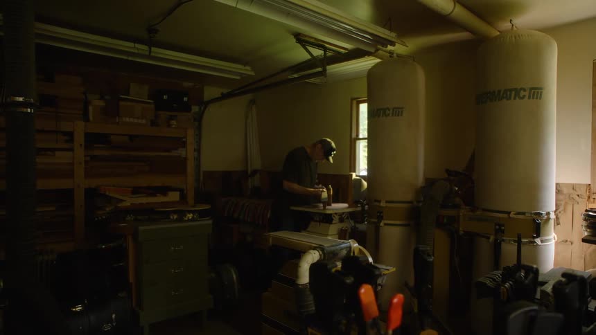 Wide shot of a skilled craftsman sanding a piece of wood in a dimly lit, professional home workshop